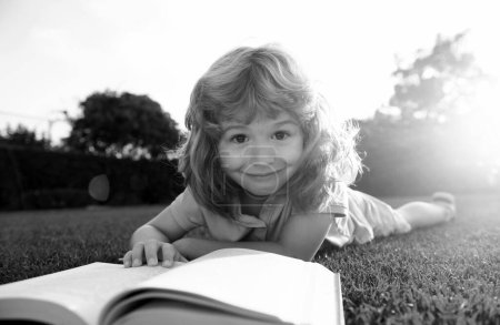 Foto de Inteligente inteligente chico leyendo libro sobre hierba verde - Imagen libre de derechos