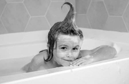 Téléchargez les photos : Enfant avec mousse de shampooing et bulles sur les cheveux prenant un bain. Visage drôle d'enfant en mousse, soin des cheveux et concept d'hygiène. Baignoire avec bulle de savon - en image libre de droit