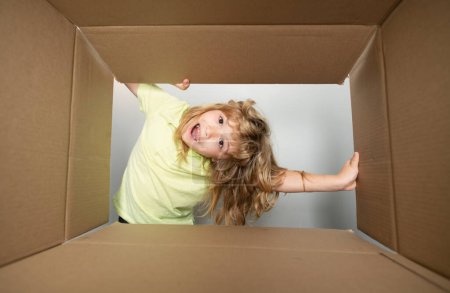 Téléchargez les photos : Kid déballer et ouvrir la boîte en carton, et regarder à l'intérieur avec un visage surprise. Ouvrir une grande boîte - en image libre de droit