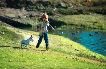 Foto de Niño y perro divertido corren en el Parque Verde. Niño pequeño compitiendo con el cachorro - Imagen libre de derechos