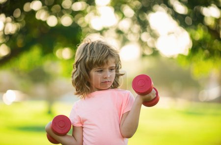 Foto de Mancuernas de fitness ejercicio para niños ejercicio al aire libre. Niño deportivo niño con mancuernas - Imagen libre de derechos