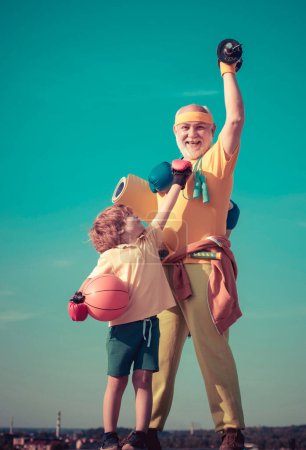 Foto de Abuelo y nieto con pelota de baloncesto y esterilla de yoga en las manos. Padre e hijo haciendo ejercicio. Día de los Padres. Padre e hijo deportistas - tiempo en familia juntos - Imagen libre de derechos