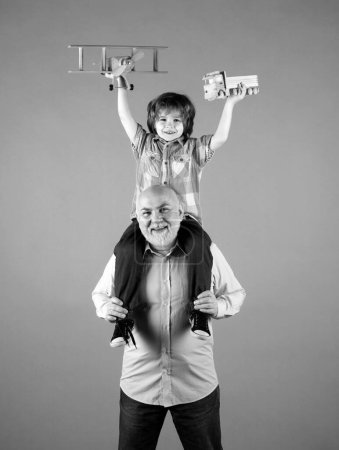 Téléchargez les photos : Jeune petit-fils et vieux grand-père avec avion jouet et camion jouet en bois. Hommes génération grand-père et petit-enfant. Aîné parent âgé avec enfant - en image libre de droit