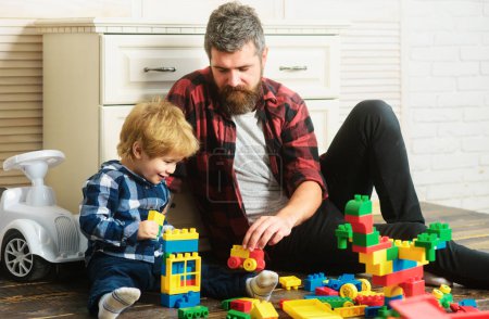 Foto de Father takes part in game with son playing on floor holding toy cars. Father and son create toys from bricks. Dad and kid build of plastic blocks - Imagen libre de derechos