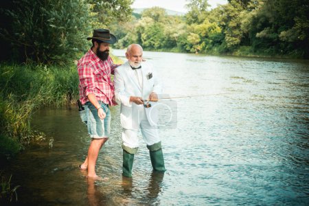 Téléchargez les photos : Deux hommes amis pêcheur pêche sur la rivière. Vieux père et fils avec canne à pêche au bord de la rivière. Activités récréatives - en image libre de droit