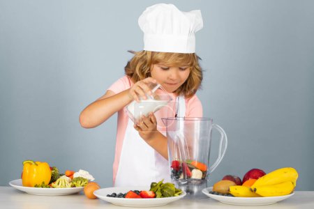 Téléchargez les photos : Portrait d'enfant chef dans un chapeau de cuisinier faire smoothie milk shake. Cuisson à la maison, gamin préparant des aliments à partir de légumes et de fruits. Une alimentation saine - en image libre de droit