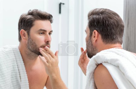 Hispanischer Mann mittleren Alters, der in Spiegel, Gesichtshaut und Stoppeln blickt. Männliche Schönheitspflege. Hautpflege, home spa. Schönheitsporträt eines schönen Mannes. Spa-Modell, feuchtigkeitsspendende Pflegecreme