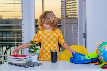 Photo for School child 7-8 years old puts school supplies in a backpack go back to school. Little student doing homework at home - Royalty Free Image