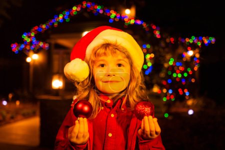 Foto de Feliz Año Nuevo y Feliz Navidad. Retrato de niños felices, niño disfrutando de vacaciones de invierno en el patio delantero. Casa decorada con guirnaldas - Imagen libre de derechos