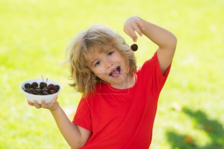 Photo for Cherry fot kids. Happy kid eating ripe, sweet, juicy, fresh cherries. Child in red t-shirt holding cherries. Concept of healthy summer food - Royalty Free Image