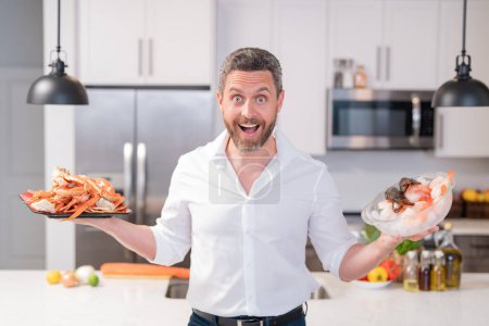 Téléchargez les photos : Homme dans la cuisine moderne préparant du saumon de poisson. Beau homme cuisine du poisson frais saumon fruits de mer crabe et crevettes et homard dans la cuisine à la maison - en image libre de droit