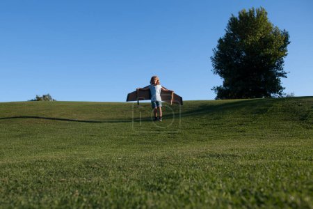 Photo for Caucasian kid playing with toy plane on sky background outside on grassy summer hill. Dreaming about happy future concept. Little boy dream of flying, traveling on plane, fantasies - Royalty Free Image