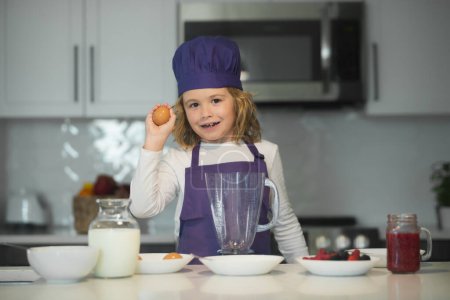 Téléchargez les photos : Enfant cuisinier. Un enfant chef tient des œufs. L'enfant prépare la pâte, fait cuire les biscuits dans la cuisine - en image libre de droit