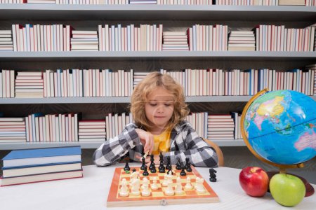 Téléchargez les photos : Les enfants jouent aux échecs. Un enfant intelligent qui pense aux échecs. Portrait d'un enfant intelligent avec un échiquier. Garçon jouer aux échecs - en image libre de droit