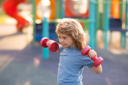 Photo for Kids sport training on playground outdoor. Kid raising a dumbbell. Cute child training with dumbbells. Kids fitness. Kid boy exercising with dumbbells. Healthy kids - Royalty Free Image
