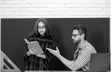 Photo for Pupil and teacher reading book. Portrait of schoolkids and teacher talking at school lesson doing homework writing and reading at school - Royalty Free Image