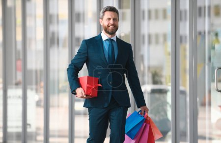 Téléchargez les photos : Homme d'affaires tenant des sacs à provisions et marchant dans un magasin. Faire du shopping et payer. Magasins concept de shopping - en image libre de droit