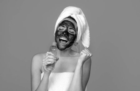 Téléchargez les photos : Excité étonné belle femme avec la procédure faciale de boue cosmétique, concept de santé spa. Soins de la peau traitement de beauté. Serviette sur la tête. Boue minérale médicale - en image libre de droit
