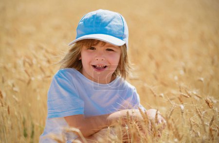 Foto de Niño feliz en el campo de trigo al aire libre. Lindo niño sonriente caminando por el campo de trigo - Imagen libre de derechos