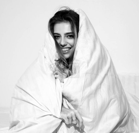 Foto de Hermosa joven envuelta en una suave manta sentada en la cama. Despertar por la mañana - Imagen libre de derechos