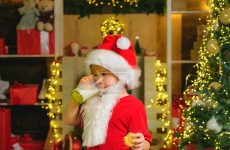 Téléchargez les photos : Portrait du Père Noël Boire du lait dans du verre et tenir des biscuits. Petit Père Noël avec barbe et moustache. Père Noël en chapeau de Père Noël. Noël pour enfant - en image libre de droit