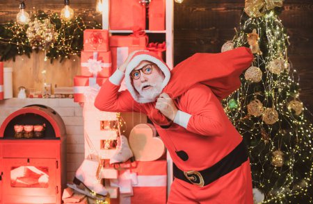 Téléchargez les photos : Funny Santa tenir cadeau de Noël. Ambiance de Noël. Portrait de beau Père Noël homme à l'intérieur avec cadeau de Noël. - en image libre de droit