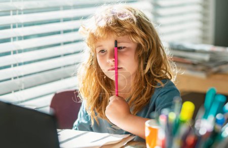 Photo for Tired serious schoolboy while doing homework. Portrait school kid siting on table doing homework. Funny child girl doing homework writing and reading at home. Little student at desk in school - Royalty Free Image