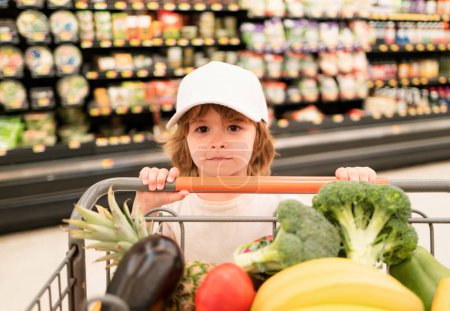 Téléchargez les photos : Un garçon fait du shopping dans un supermarché. Chariot de retenue pour enfant drôle de client, magasinage au supermarché, épicerie - en image libre de droit