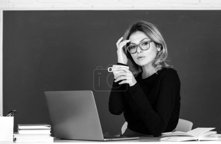 Téléchargez les photos : Jeune enseignante ou étudiante buvant du café avec cahier sur un tableau blanc - en image libre de droit