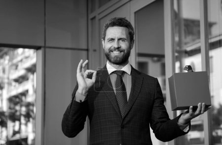 Téléchargez les photos : Portrait d'homme d'affaires avec ok signe en costume montrant boîte cadeau - en image libre de droit