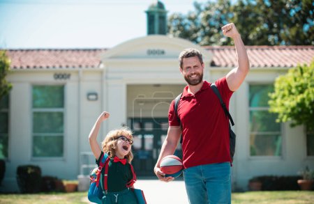 Photo for Parent and pupil of primary school go hand in hand. Teacher in t-shirt and cute schoolboy with backpack near school park. - Royalty Free Image