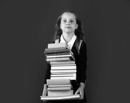 Téléchargez les photos : Journée de la connaissance, Souriante petite écolière avec sac à dos tenir des livres sur le tableau vert. Concept de style de vie de l'enfance. Éducation à l'école - en image libre de droit