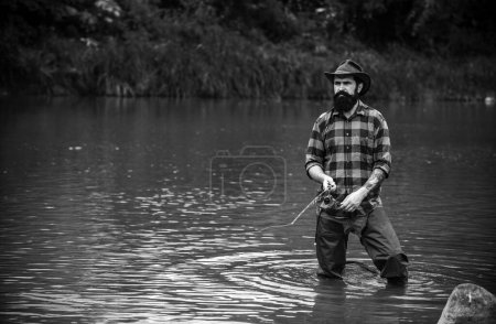 Téléchargez les photos : Un jeune homme pêche. Pêcheur avec canne, moulinet tournant sur le bord de la rivière. Homme attrapant des poissons, tirant la canne tout en pêchant sur le lac. Nature sauvage. Le concept de escapade rurale - en image libre de droit