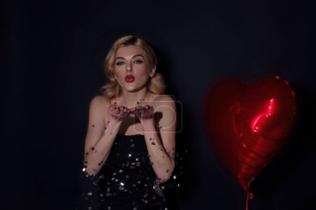 Photo for Sexy blonde woman blowing confetti. Love and valentine beauty girl. Beautiful girl holding heart shape balloon. Sexy woman hold red heart symbol of Valentines day and love - Royalty Free Image