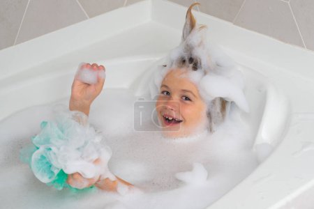 Photo for Soap on child head. Child face in foam. Kid washing with a bubbles in bath. Cute child bathes, lying in a white bath with foam from soap and shampoo - Royalty Free Image