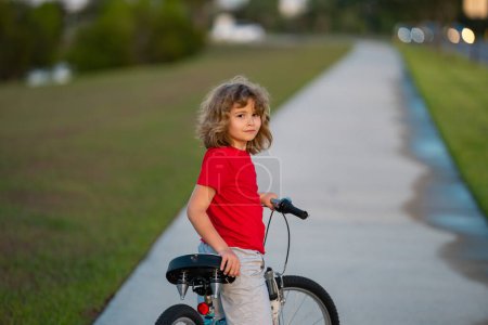 Photo for Kid boy riding a bike in summer park. Child drive a bike on a driveway outside. Kid riding bikes. Child on bike outdoor. Kid bicycling bike on american neighborhood - Royalty Free Image