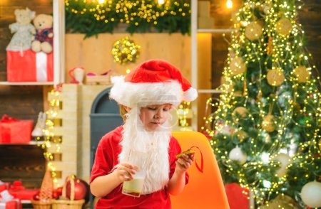 Téléchargez les photos : Le Père Noël prend un cookie la veille de Noël comme cadeau de remerciement pour laisser des cadeaux. Nourriture et boisson de Noël. Enfant de Noël - en image libre de droit