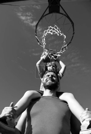 Photo for Father and son playing basketball. Father carrying his son on shoulders on the basketball court - Royalty Free Image