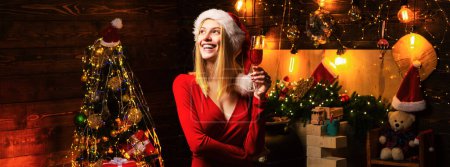 Téléchargez les photos : Santa femme tenant un verre de champagne célèbre Noël à la maison chambre décorée - en image libre de droit