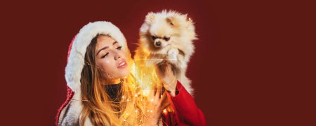 Téléchargez les photos : Portrait d'une belle femme avec chien célébrer les vacances de Noël d'hiver tenir chiot chien sur fond rouge. Nouvel An chiot - en image libre de droit