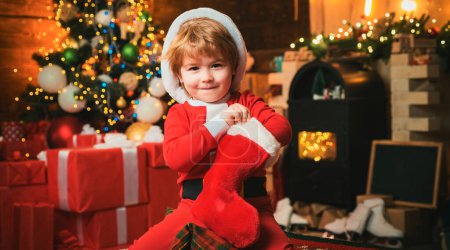 Téléchargez les photos : Un enfant a reçu un cadeau en chaussette de Noël. Concept de bas de Noël. Enfant garçon tenir cadeau de Noël - en image libre de droit