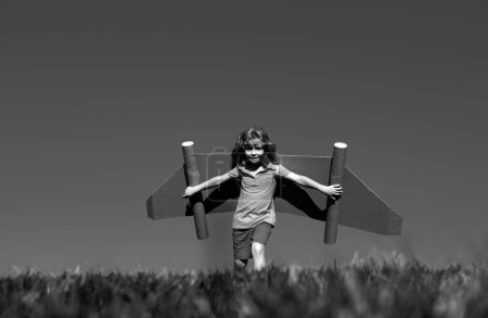 Téléchargez les photos : Enfant avec super-héros jet pack. Enfant pilote sur fond de ciel estival. Garçon avec avion en papier, Avion jouet avec ailes en carton, Imagination, Liberté des enfants - en image libre de droit