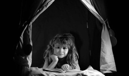 Photo for Child boy in kids tent reading book. Serious child reading books, looks serious and concentrated, playing at home, reads story or fairytales - Royalty Free Image