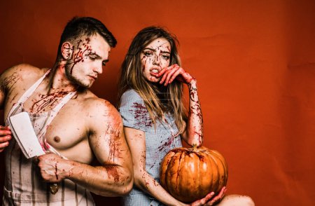 Téléchargez les photos : Couple fou Halloween sur fond rouge isolé. Couple dans le sang. La faim animale. Un homme fort portant un tablier de boucher avec des taches de sang. Joyeux Halloween - en image libre de droit
