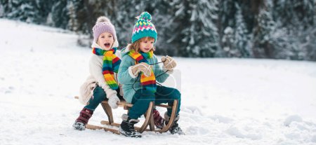 Photo for Kids ride on a wooden retro sled on a winter day. Active winter outdoors games. Friends children boy and girl sledding in winter. Kids sibling riding on snow slides in winter - Royalty Free Image