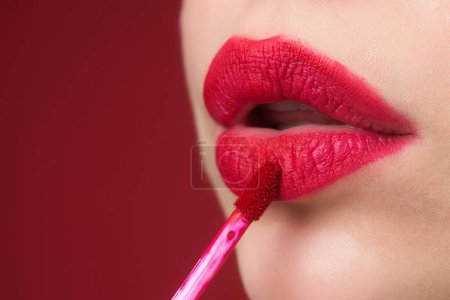 Photo for Applying lipstick, macro. Painting lips with bright lipstick, close up. Pampering, lips correction concept. Glossy lipstick on full plump lip. Woman hand applying lipstick. Lip balm - Royalty Free Image
