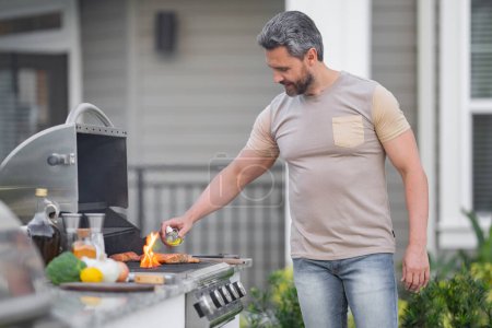 Photo for Hispanic man cooking on barbecue in the backyard. Chef preparing barbecue. Barbecue chef master. Man in apron preparing delicious grilled barbecue food, bbq meat. Grill and barbeque - Royalty Free Image