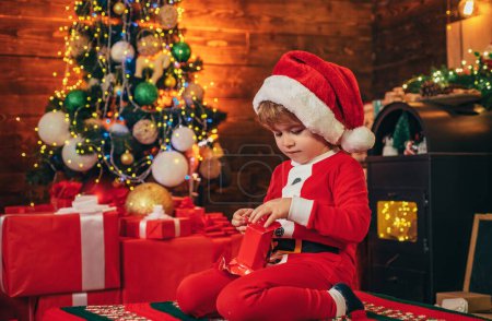 Foto de Niño pequeño decorando árbol de Navidad y regalos de apertura. Año Nuevo. En Navidad. Niña elfa. Venta de compras de invierno. Un regalo sorpresa de Año Nuevo. Feliz y brillante navidad - Imagen libre de derechos
