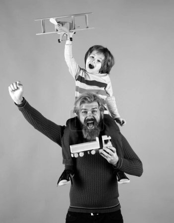 Foto de Padre e hijo. Aviador piloto infantil con sueños de avión de viajar sobre fondo azul. Retrato de padre feliz dando hijo paseo a cuestas sobre sus hombros y mirando hacia arriba - Imagen libre de derechos