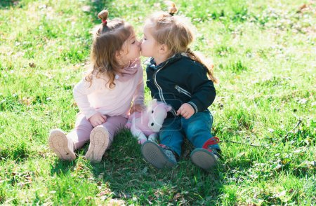 Foto de A los niños lindos les encanta. Niña besando a niño al aire libre en el parque. Niños en el hermoso campo verde de primavera - Imagen libre de derechos